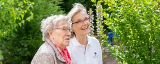 Im Garten: eine Pflegerin zeigt einer Bewohnerin etwas (nicht sichtbar)