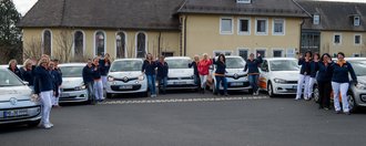 Gruppenfoto mit KFZ-Fahrzeugflotte: Frauen die vor ihren Fahrzeugen stehen und winken